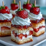 Delightful mini strawberry shortcake bites on skewers, topped with whipped cream and fresh berries.
