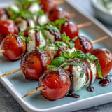 Mini Caprese skewers bursting with ripe tomatoes, mozzarella, and basil, drizzled.