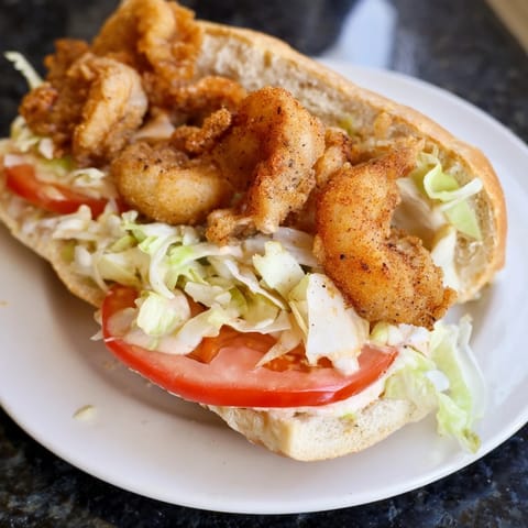 A close-up shot of a Shrimp Po Boy revealing golden, crispy shrimp and creamy mayo filling.
