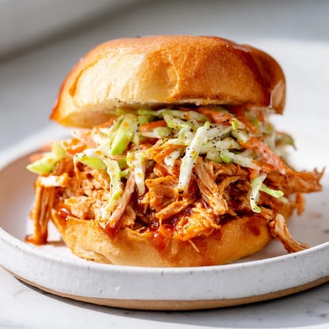 Smoky, tender BBQ chicken sandwich, served warm, promising a delicious mix of textures and savory flavors.