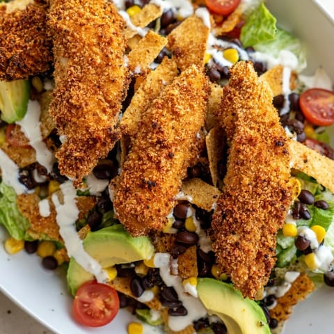 A fresh Crispy Chicken Taco Salad topped with tortilla strips, black beans, corn, avocado, and cheese.