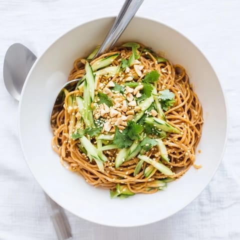 A vibrant bowl of spicy sesame noodle salad garnished with toasted sesame seeds and peanuts.  