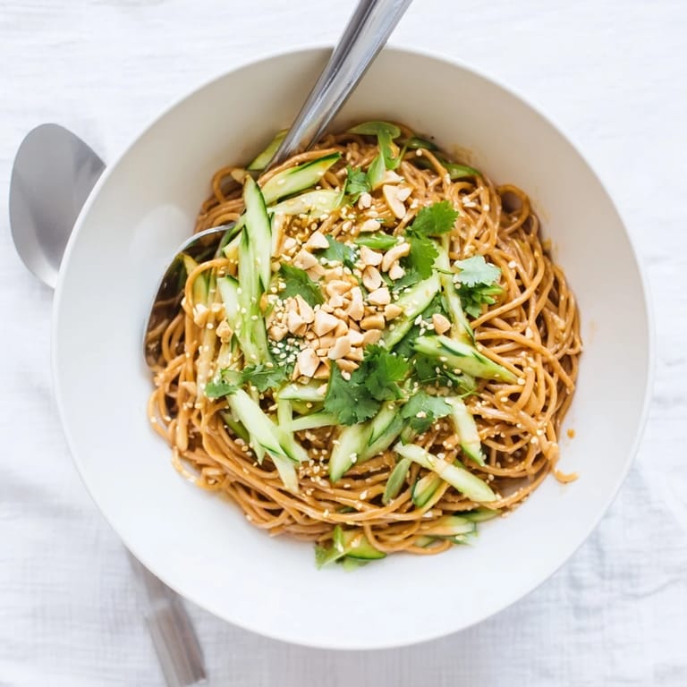 A vibrant bowl of spicy sesame noodle salad garnished with toasted sesame seeds and peanuts.  