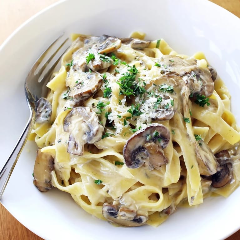 Creamy Mushroom Alfredo is tossed with al dente fettuccine, garnished with fresh parsley and extra Parmesan, ready to be served on a white plate.
