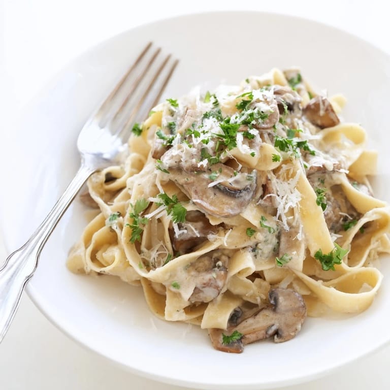 Creamy Mushroom Alfredo reveals silky cream sauce clinging to noodles, with visible mushroom slices and a wooden spoon resting beside the skillet.