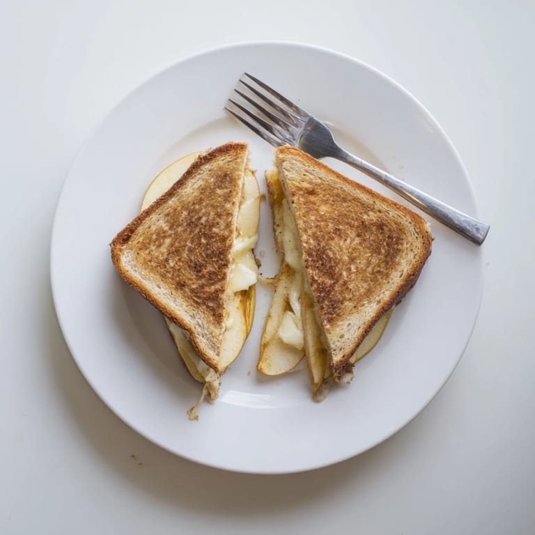 Two slices of golden, buttery grilled cheese with thin apple layers, ready to be enjoyed with a hot bowl of soup.